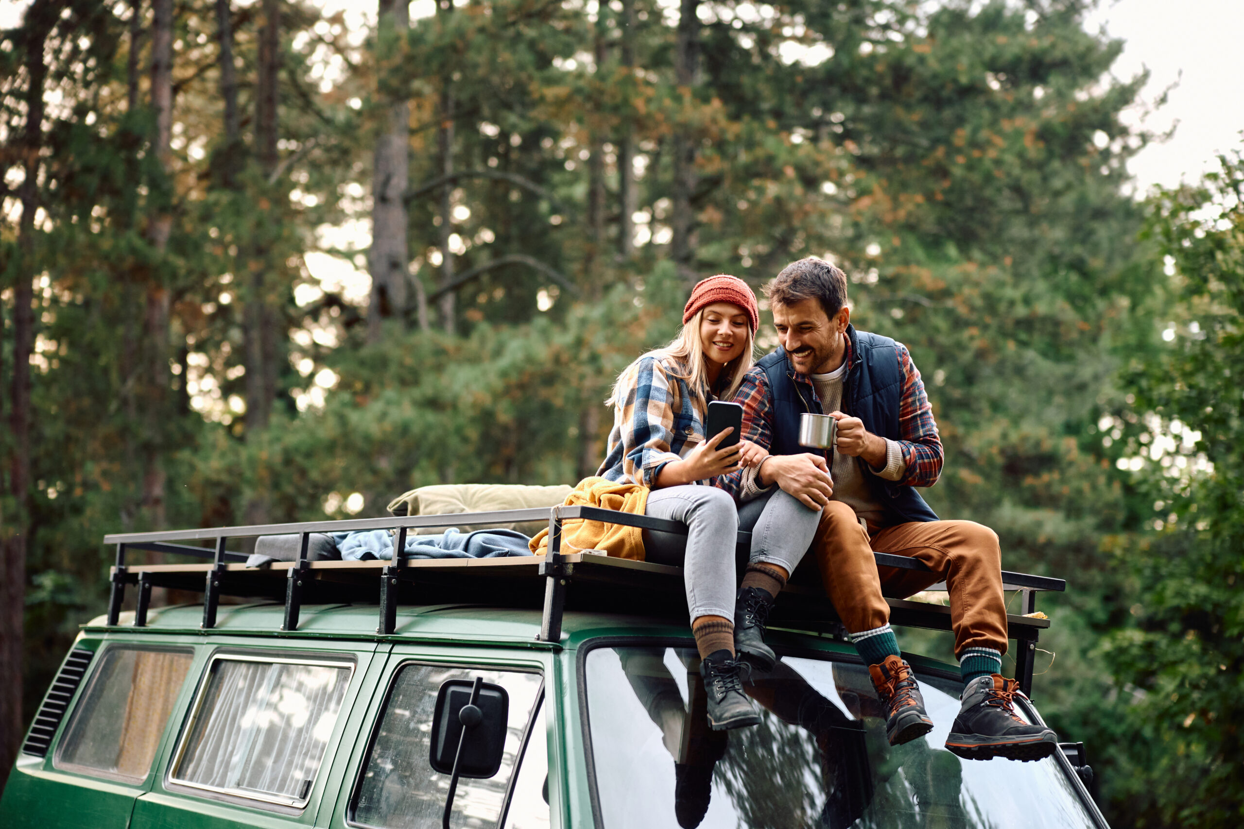 Couple assis sur le toit de son van aménagé en pleine nature